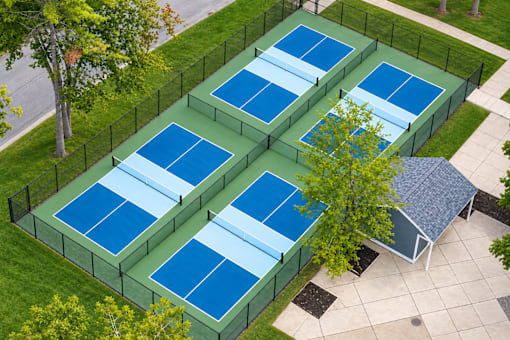A tennis court is surrounded by a fence and has a small pavilion.