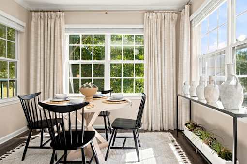 A dining room with a table set for two and a window with curtains.