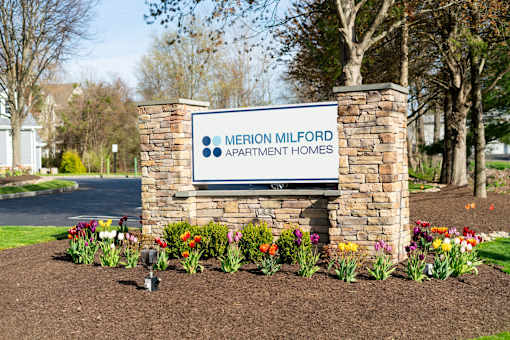A sign for Merion Milford Apartment Homes is surrounded by flowers.