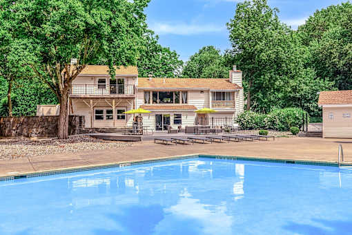 A swimming pool in front of a house surrounded by trees.