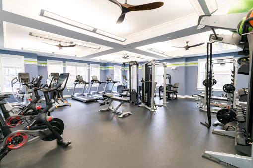 a gym with cardio machines and weights on the floor and a ceiling fan