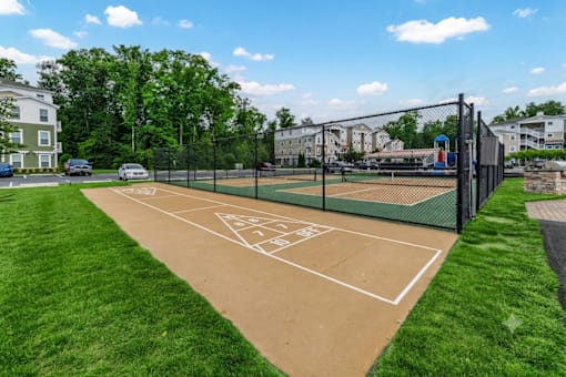 A tennis court surrounded by a fence and green grass.
