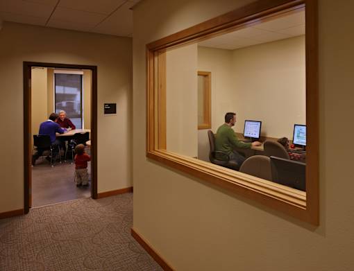 A man is sitting in front of a computer in a room with a mirror on the wall.