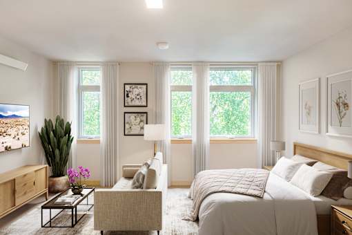 A well-lit bedroom with a large bed, a couch, a coffee table, and a painting on the wall.