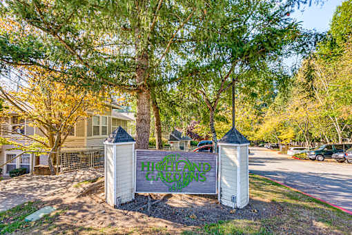 A sign that says "Hillcrest Gardens" is in front of a tree.