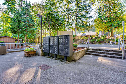 A large grey electrical box sits in the middle of a paved area with a tree in the background.