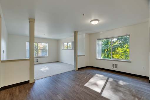 A large empty room with wooden floors and a window showing green trees outside.