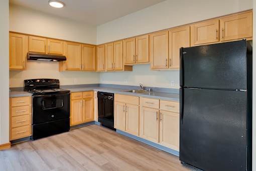 A black refrigerator is in the corner of a kitchen with wooden cabinets.