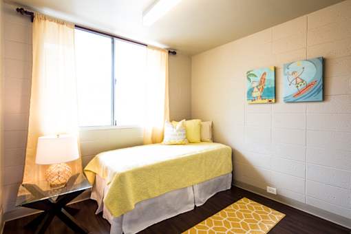 A bedroom with a bed, a table with a lamp, and two paintings on the wall.