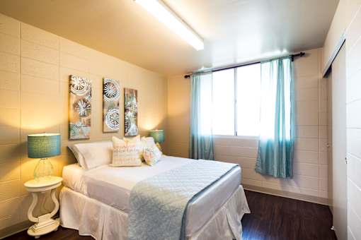 A bedroom with a bed, a nightstand with a lamp, and a window with curtains.