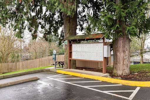 A parking lot with a wooden structure and a bench under a tree.