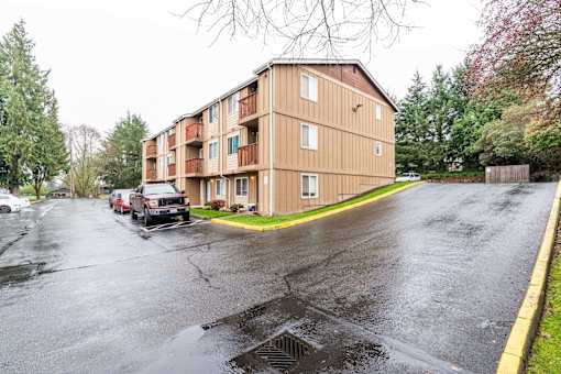 A large apartment building is situated on a street with a parking lot in front.