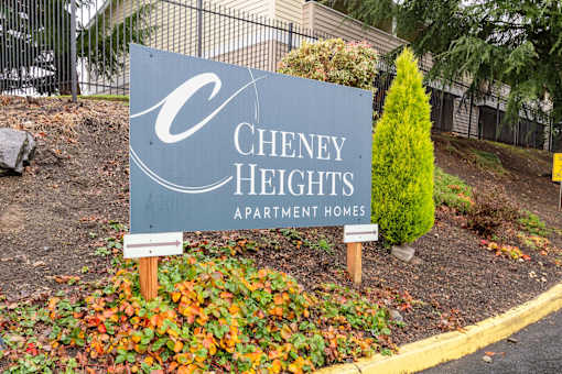 A sign for Cheney Heights Apartment Homes is displayed in front of a fence and some trees.
