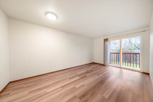 A room with wooden flooring and a window with a view of a fence.