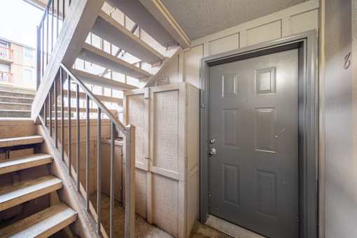 A grey door is in a hallway with a staircase.