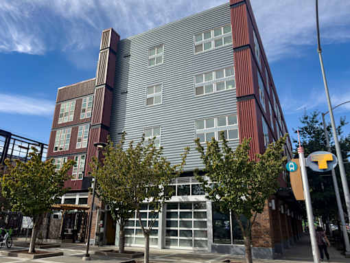 A modern building with a red and grey facade stands on a street corner.