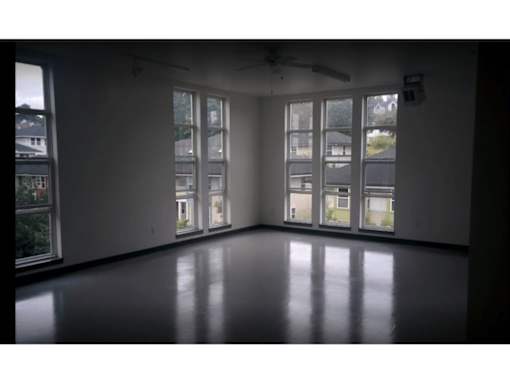 A room with a ceiling fan and large windows overlooking a residential area.