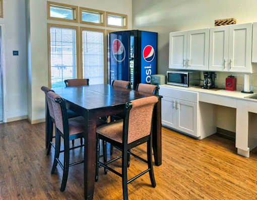 A dining table with chairs and a Pepsi fridge in the background.