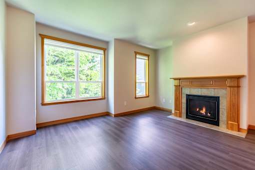 A large empty room with a fireplace and two windows.