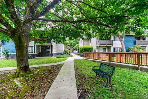 A green bench is on the grass next to a sidewalk.