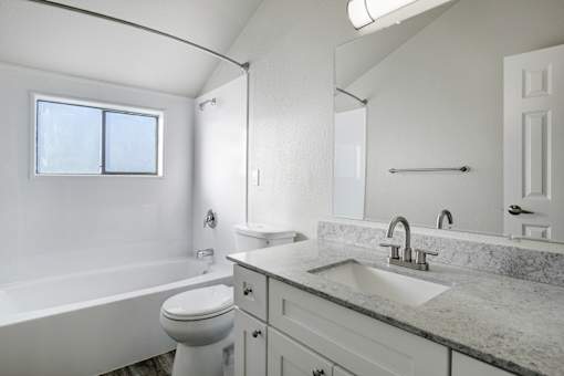 A white bathroom with a marble countertop and a window.