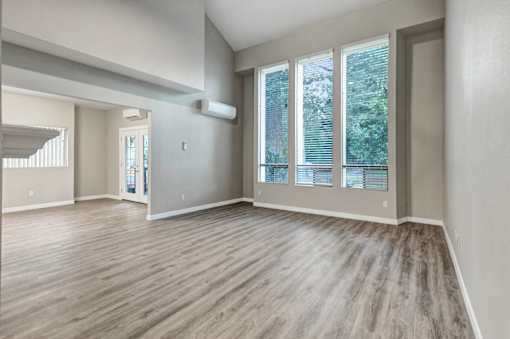 A spacious room with wooden flooring and large windows.