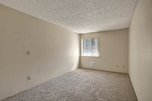 A room with a carpeted floor and a window with blinds.