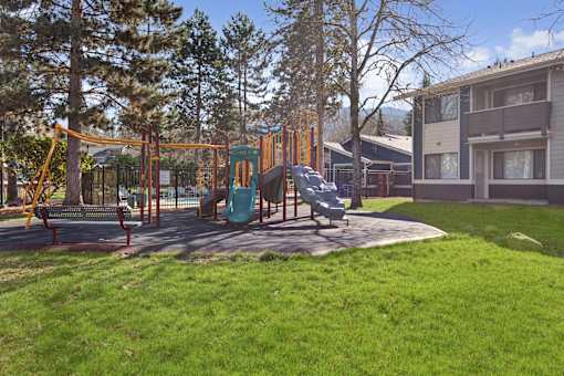 A playground with a swing set and a slide in the foreground and apartment buildings in the background.