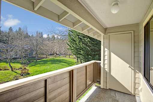 A balcony with a view of a green lawn and trees.