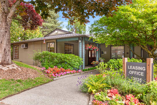 A leasing office is located in a building surrounded by greenery and flowers.