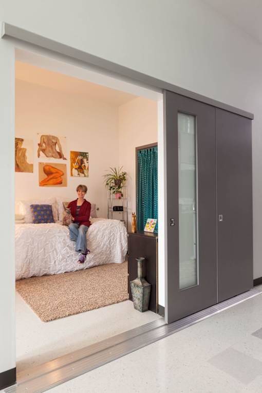 a woman sits on a bed in a bedroom with grey sliding doors
