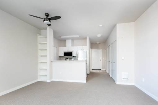 an empty living room with a kitchen and a ceiling fan