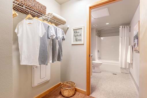 A white laundry room with clothes hanging up and a toilet in the background.