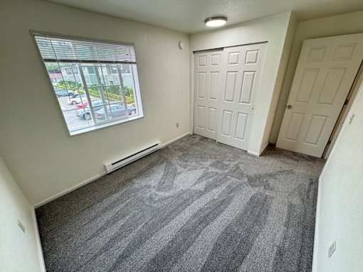 A room with a carpeted floor and a window overlooking a parking lot.