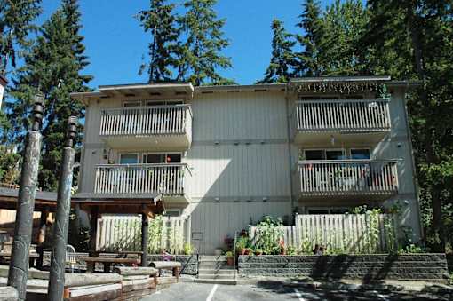 A white building with balconies is surrounded by trees.