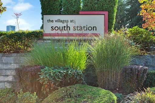 A sign that says "The Villages at South Station" is surrounded by plants.