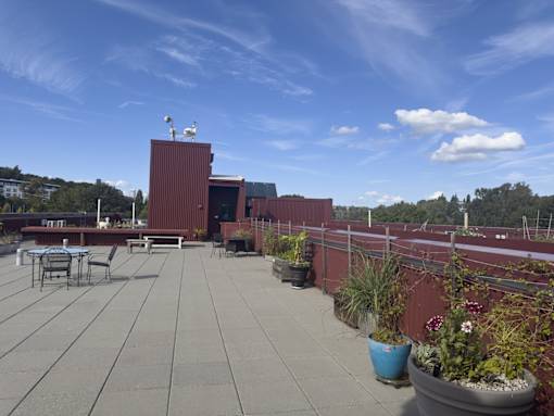A rooftop patio with a table and chairs and a red building in the background.