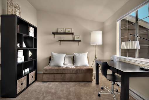 A modern living room with a brown sofa, a black desk, and a black bookshelf.