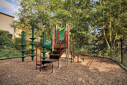 A playground with a red slide and green climbing frame.