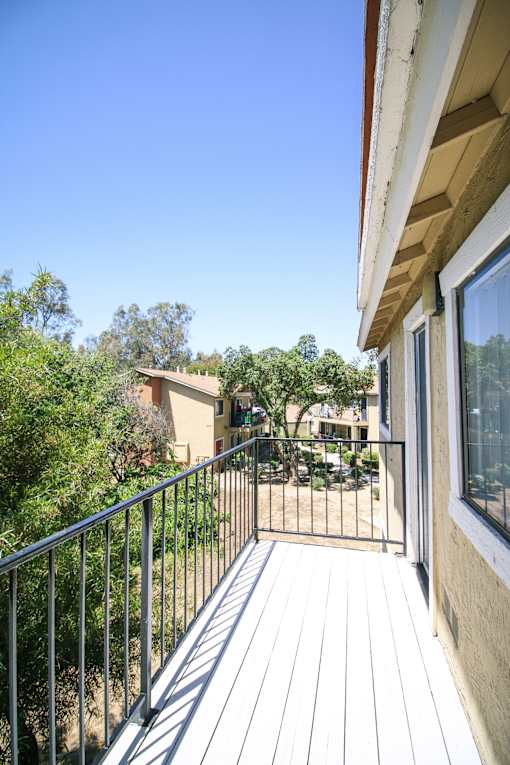 A balcony with a metal railing and a view of a building and trees.