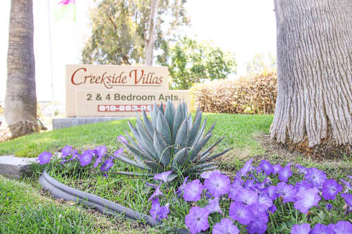 A sign for Creekside Villas with a phone number and a picture of a tree.
