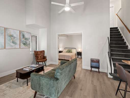 A living room with a green velvet sofa, a wooden chair, a coffee table, and a staircase.