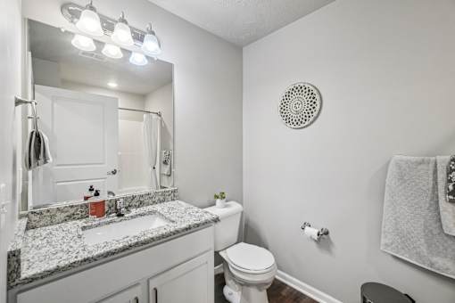 A bathroom with a toilet, sink, mirror, and towel rack.