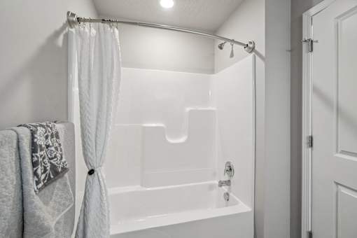 A white bathroom with a white tub and a white shower curtain.