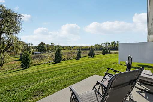 Two chairs are on a patio overlooking a green field.