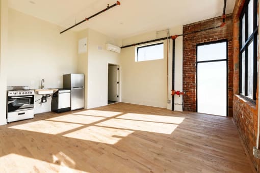 an empty living room with a kitchen and a exposed brick wall