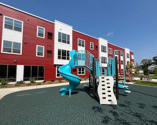 A playground with a blue slide and a white slide in front of a red and white building.