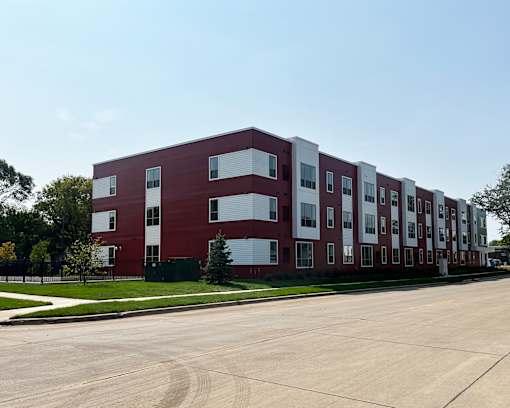 A long red and white building with a green bush in front.