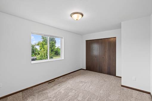 A room with a carpeted floor, a window, and a wooden door.