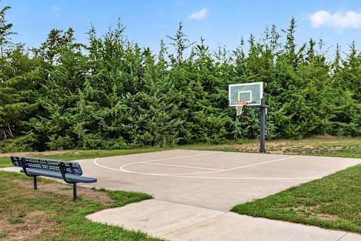 A basketball court surrounded by green trees and a bench.